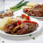 : A close-up of tender chicken pieces in a rich, dark soy-based sauce served alongside fluffy white rice, garnished with green onion slices for a pop of color