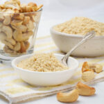 A bowl of homemade vegan parmesan cheese made from cashews, next to a glass of cashew nuts.