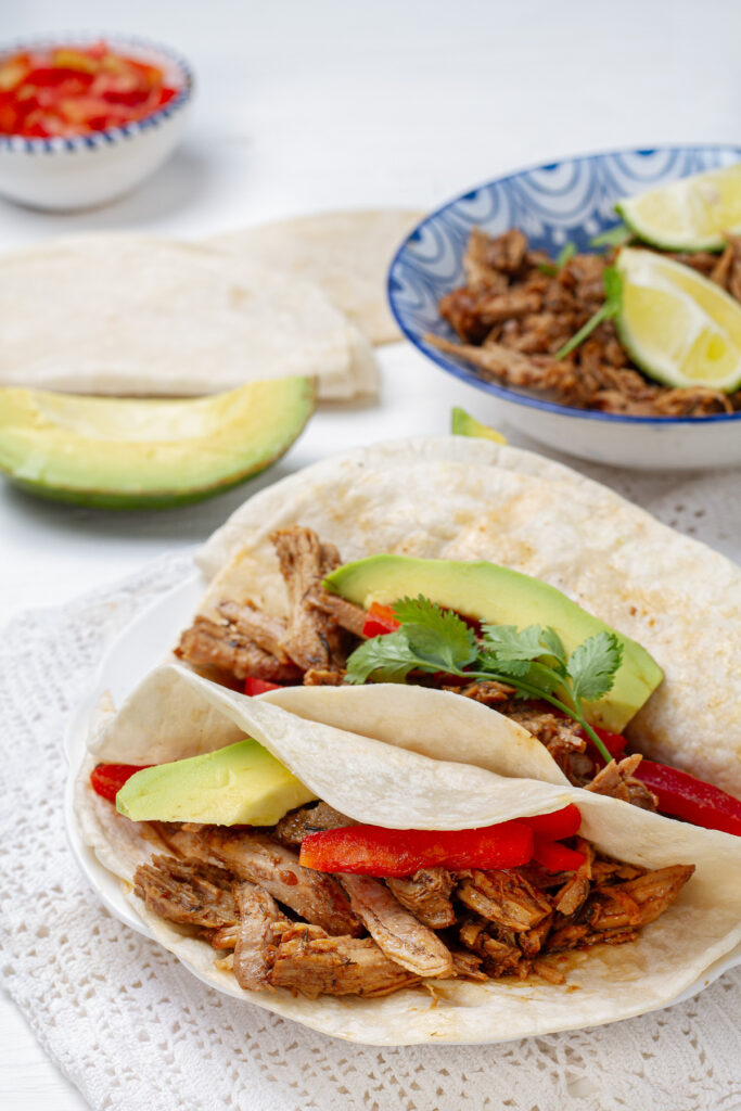 Carnitas served inside tortillas, on a white plate.