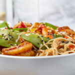 Close-up of Lo Mein noodles with stir-fried vegetables and sesame seed garnish.