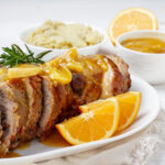 Succulent orange pork loin slices drizzled with a zesty citrus sauce, served on a white platter – perfect for holiday gatherings.