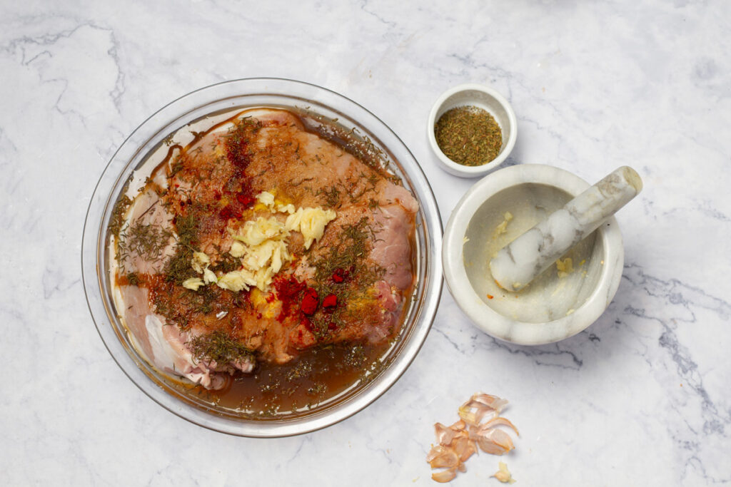 Pork shoulder marinated with seasonings, in a glass dish.