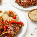 A close-up of tender chicken pieces in a rich, dark soy-based sauce served alongside fluffy white rice, garnished with green onion slices for a pop of color.