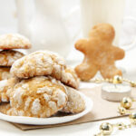 A stack of gingerbread cookies on a white plate, surrounded by holiday decorations.