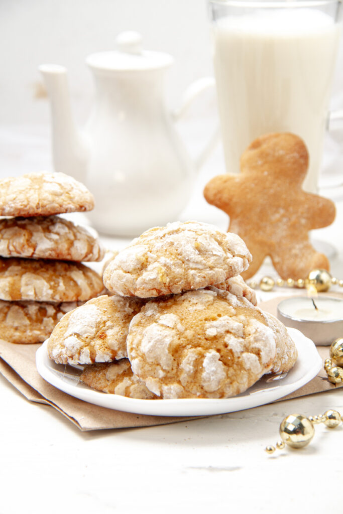 A stack of gingerbread cookies on a white plate, surrounded by holiday decorations.