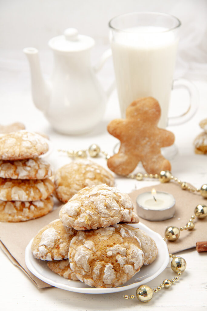 A stack of gingerbread cookies on a white plate, surrounded by holiday decorations.