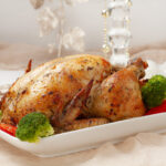 A whole roasted chicken with crispy skin, served with roasted vegetables on a white platter.