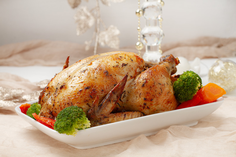 A whole roasted chicken with crispy skin, served with roasted vegetables on a white platter.