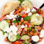 Fresh and vibrant quinoa salad in a white bowl, topped with feta, cucumbers, and herbs.