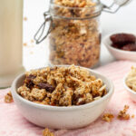 A close-up of a bowl of granola with various nuts and seeds on a white surface.