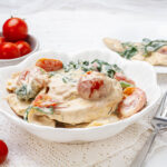 A creamy and flavorful Tuscan chicken dish topped with cherry tomatoes and spinach, served on a white plate.