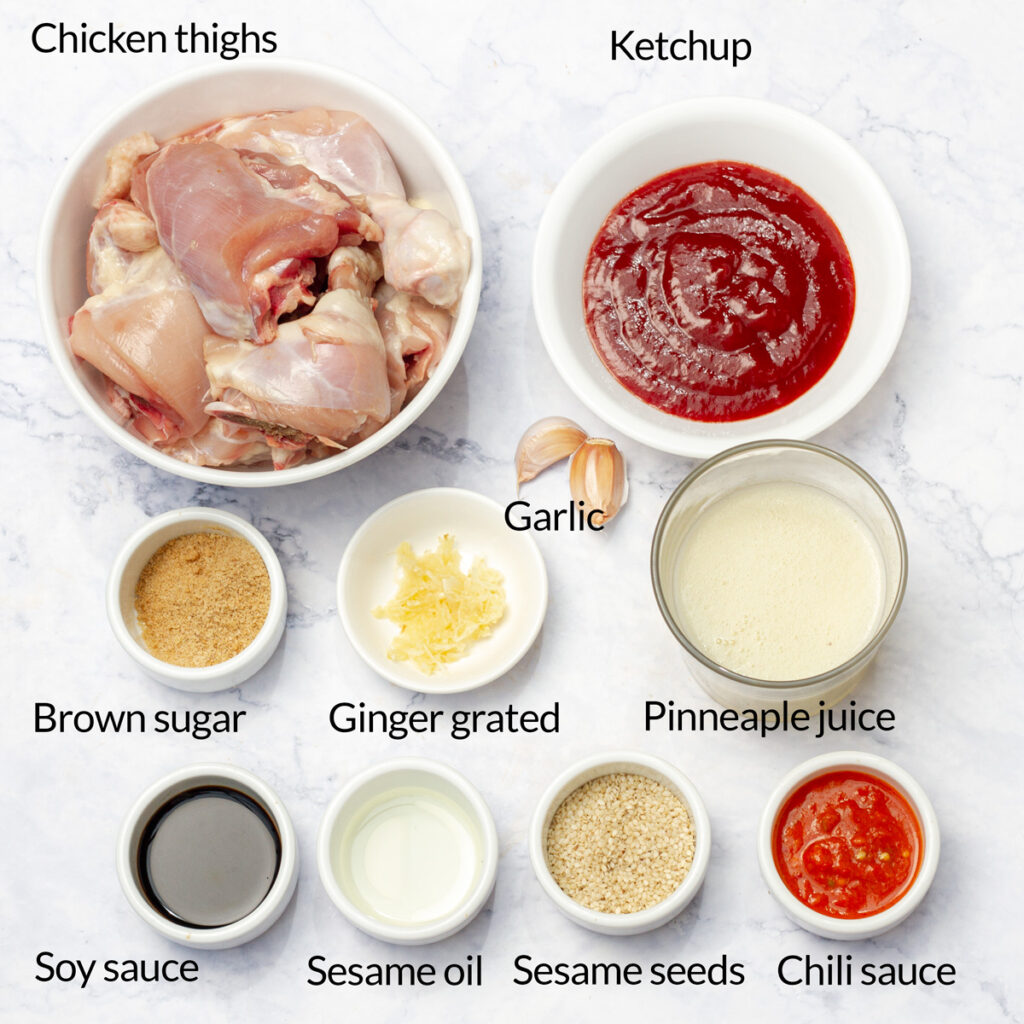 A flat lay of ingredients for making Huli Huli chicken, including chicken thighs, soy sauce, brown sugar, ginger, garlic, pineapple juice, ketchup, sesame oil, sesame seeds, and chili sauce.