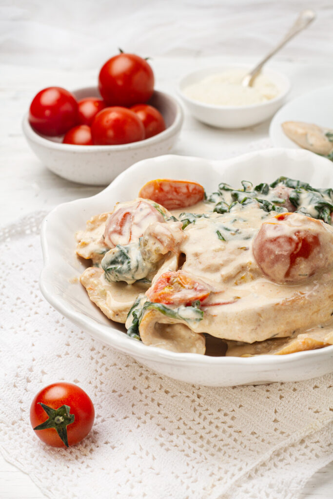 A creamy and flavorful Tuscan chicken dish topped with cherry tomatoes and spinach, served on a white plate.