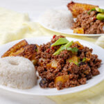 A plate of Cuban picadillo, a traditional dish made with seasoned ground beef, served with white rice, plantains, and a side salad.