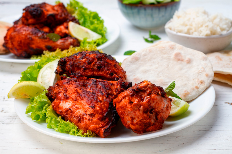 A plate of juicy tandoori chicken served with rice, naan bread, and a side salad.