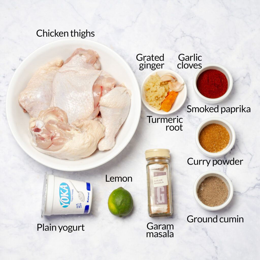 A flat lay of ingredients for making tandoori chicken, including chicken thighs, yogurt, spices, and lemon.