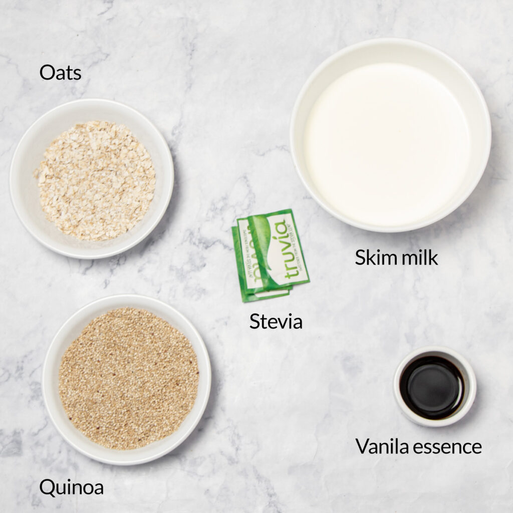 Ingredients for quinoa oatmeal breakfast: oats, quinoa, skim milk, stevia, and vanilla essence in separate white bowls on a marble countertop.